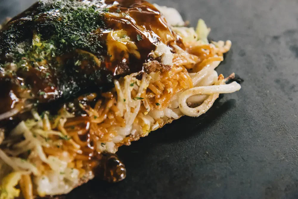 鉄板の上の、半から麺(からめんとうどんを半分ずつ)のお好み焼き