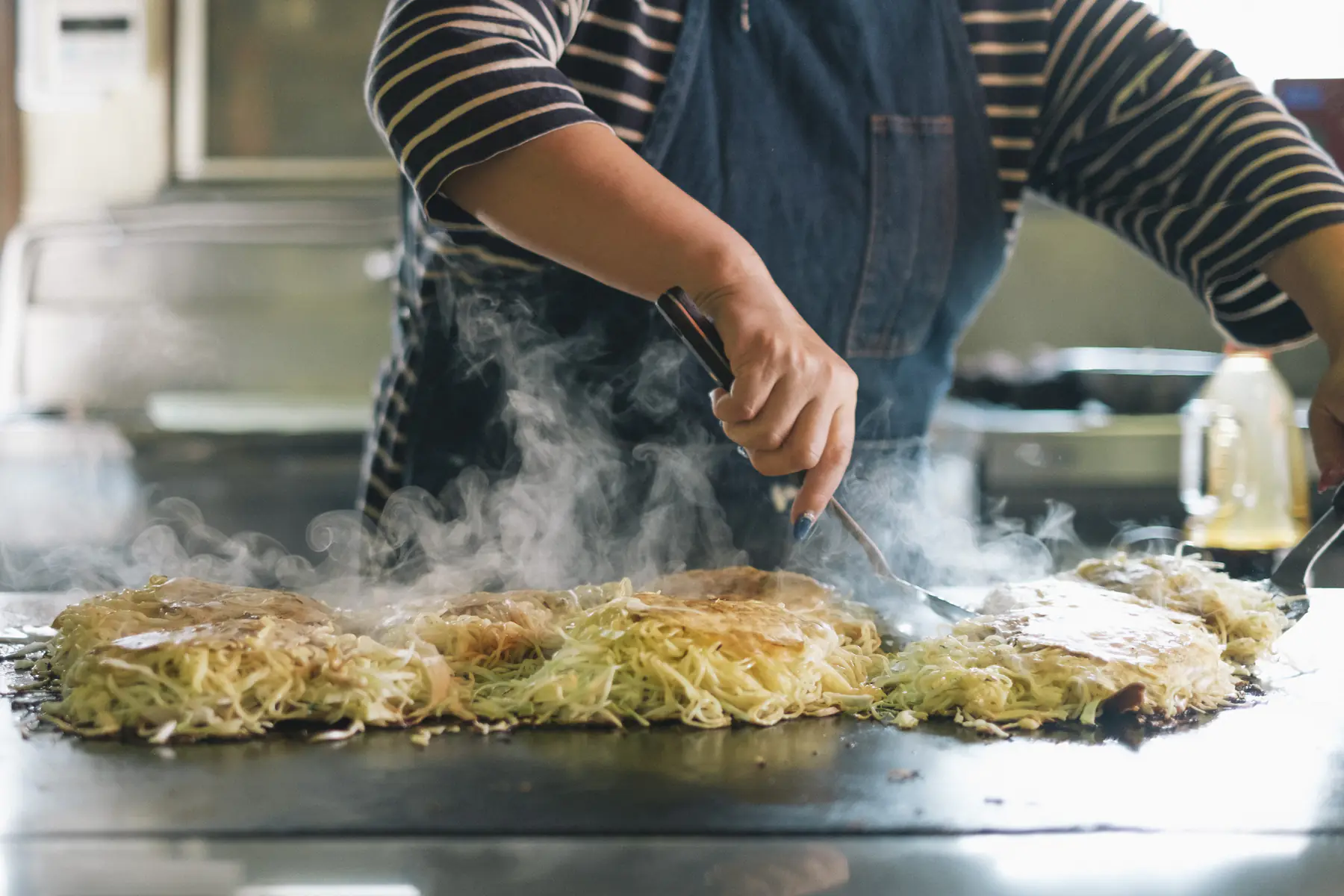 湯気の立つ鉄板で、お好み焼きを焼きあげる様子